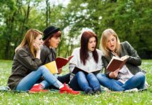 Group of young women reading books on grass in a park