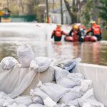 Bodies Recovered on Beach After Deadly Hurricane Sandbags stacked near a flooded street with rescue workers in a boat